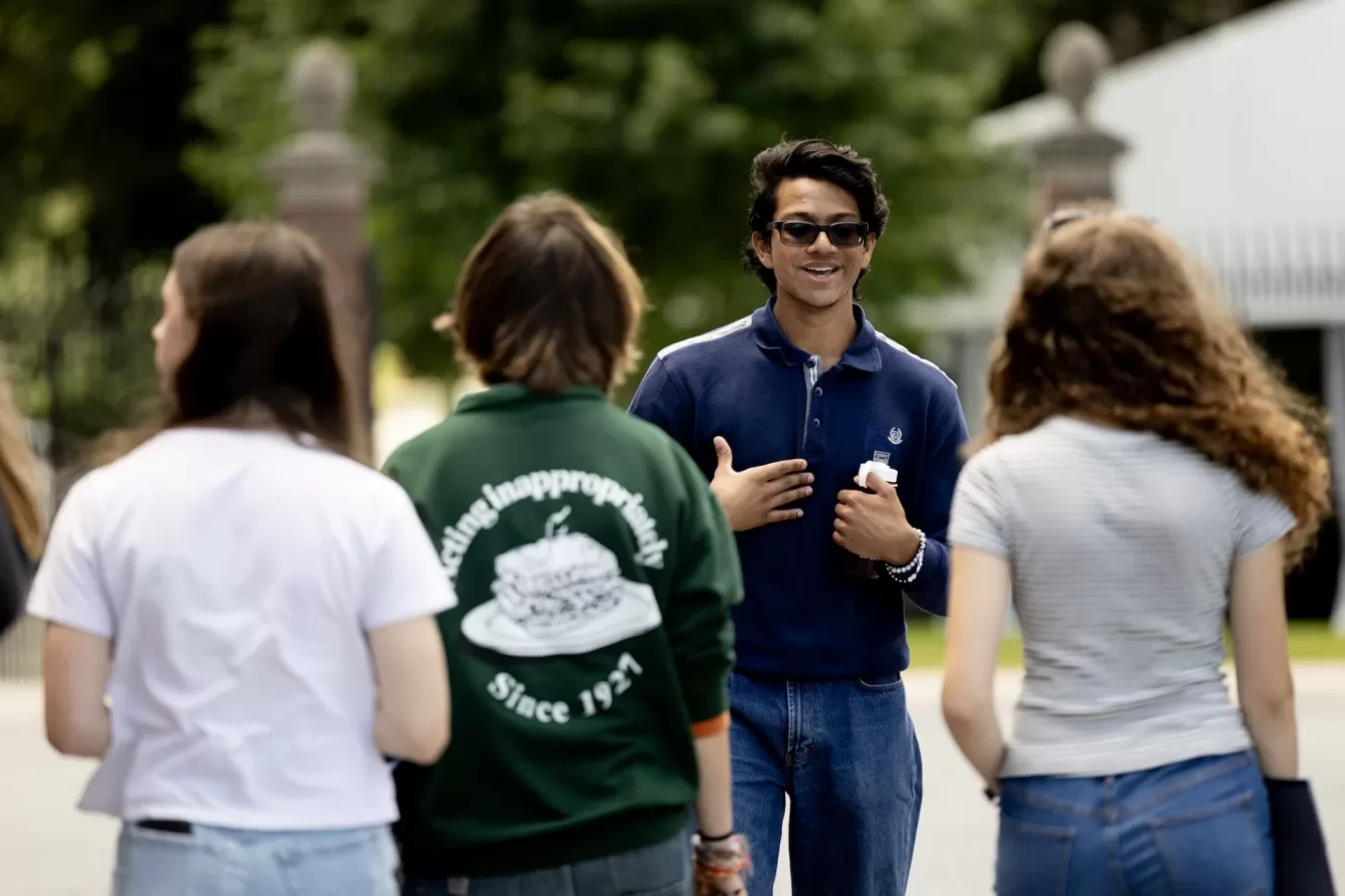 A tour guide walks backwards through campus while facing three visitors on a campus tour