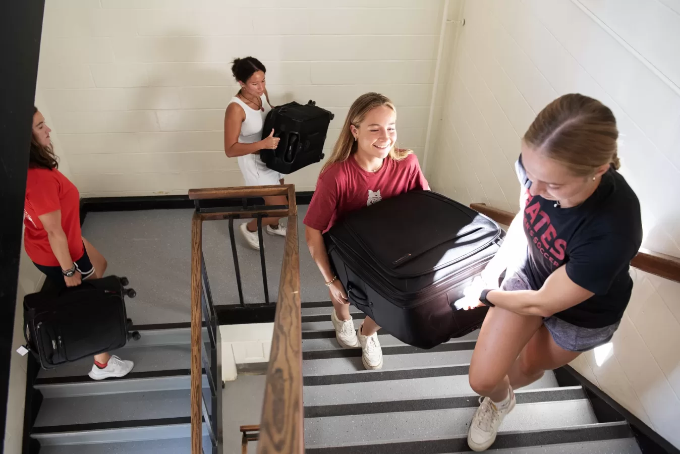 Students help carry suitcases up the stairs of a dorm on move-in day