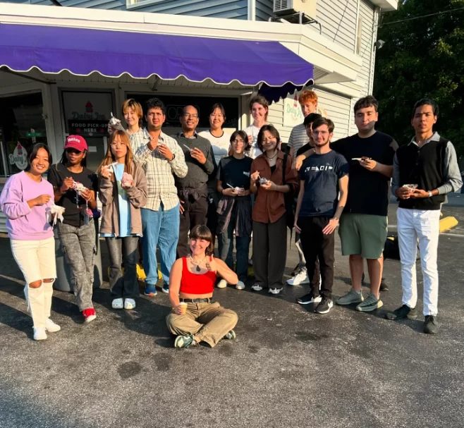 A group of people stand and sit together in front of the Dairy Joy shop eating or holding ice cream. 