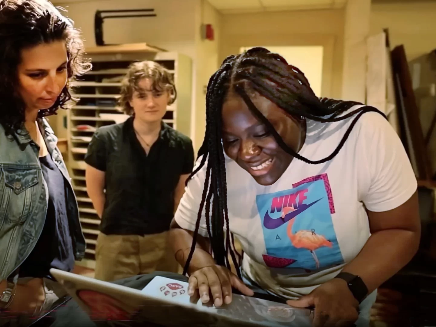 three people smiling and standing around a laptop