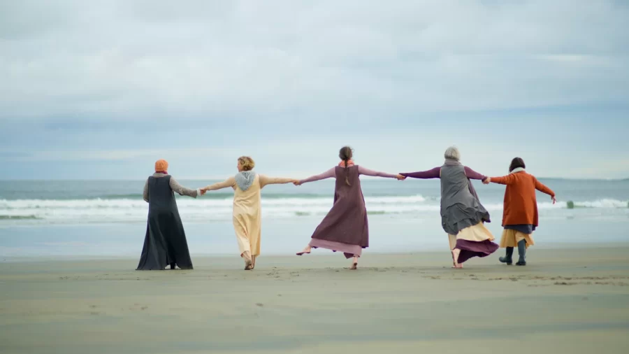 members of artist collective on beach, holding arms while moving 