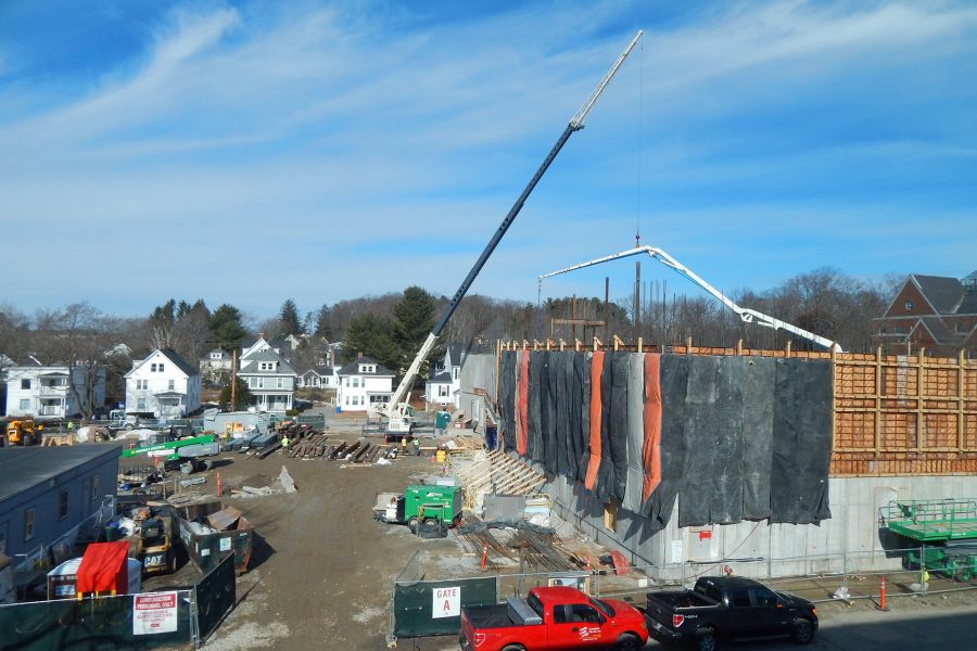 A telescoping-boom crane, left of center, hoists steel onto the second floor of the Bonney center while the boom of a concrete pump hovers over a new wall placement on the south side. (Doug Hubley/Bates College)