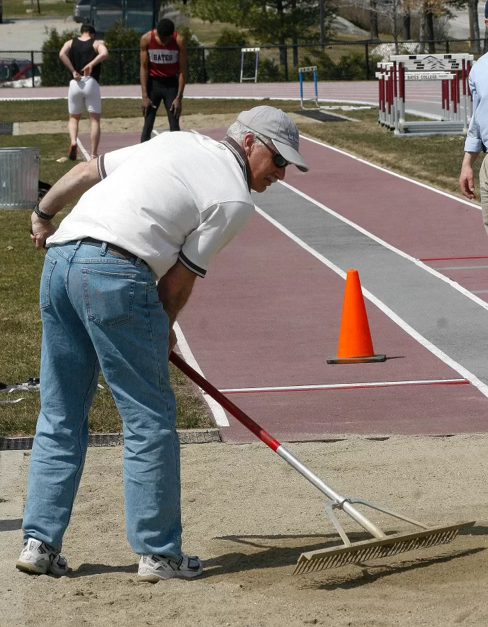 April 2007: Fereshetian raking a jumping pit, doing what coaches do, almost anything and everything. (Joe Gromelski '74)