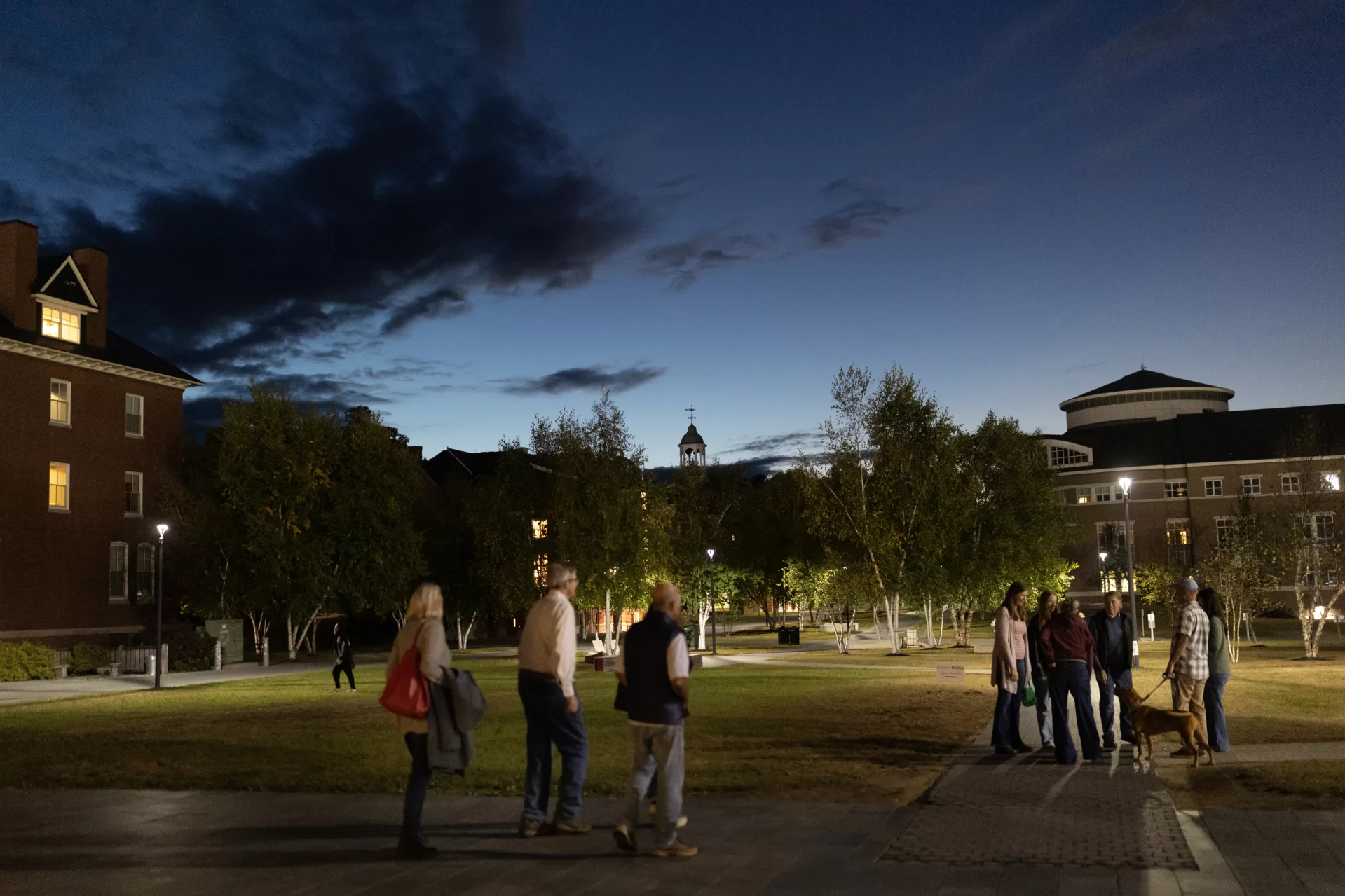 dusk on a college campus with people gathered.