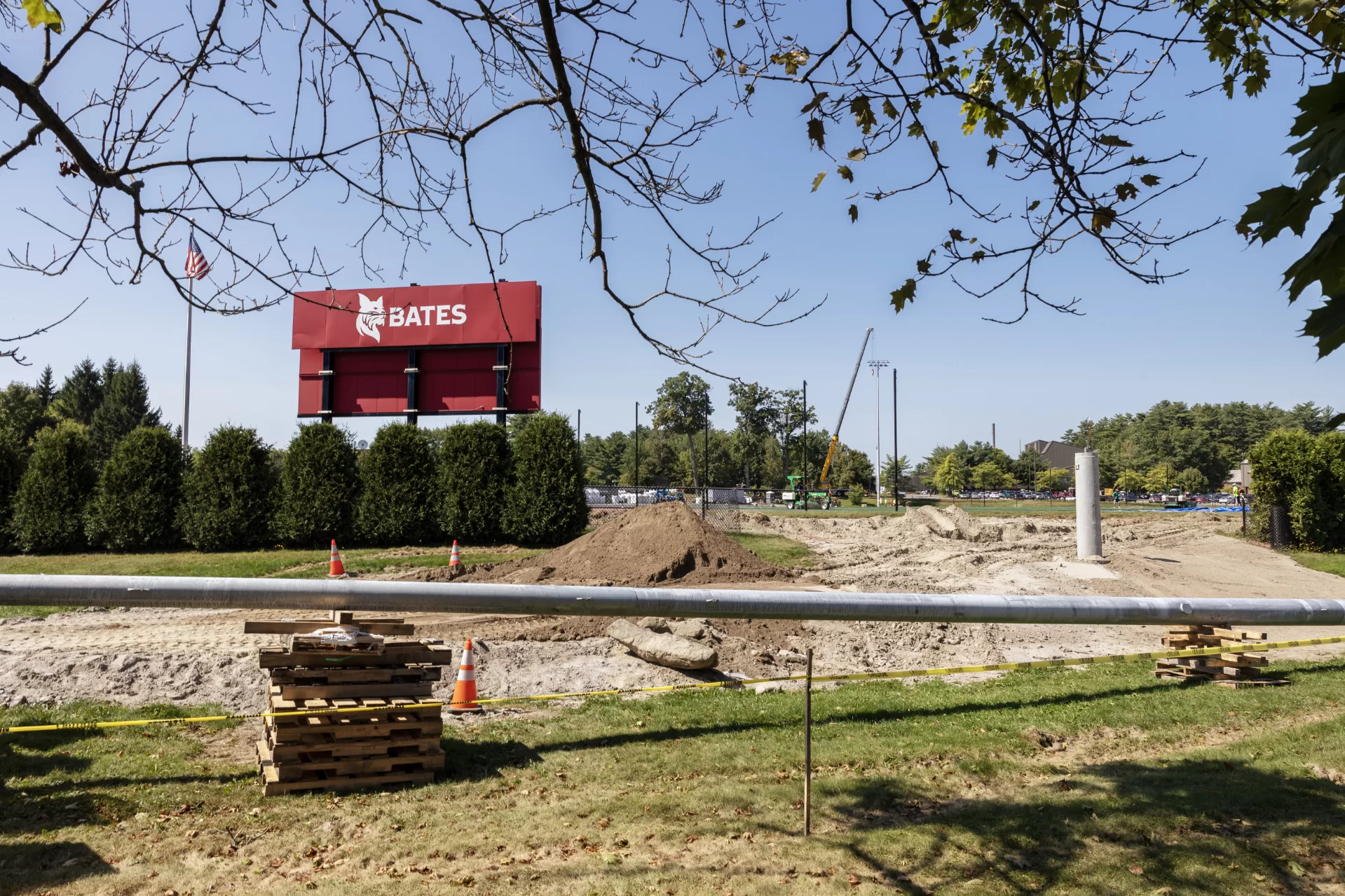 In the foreground is a pole for a Musco field light awaiting installation at Russell Street Field on Sept. 5. The concrete base for the pole stands at right. In the distance, a crane has finished erecting another field light at the opposite end of the sports complex. (Theophil Syslo | Bates College)