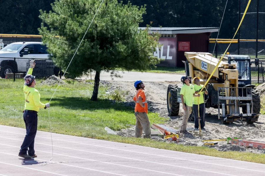 A rigger, at left, and other workers observe on Sept. 5 as a Cote Corp. crane places one of four new field lights at Russell Street Field. The lighting work was part of a summer renovation of the field. (Theophil Syslo/Bates College)