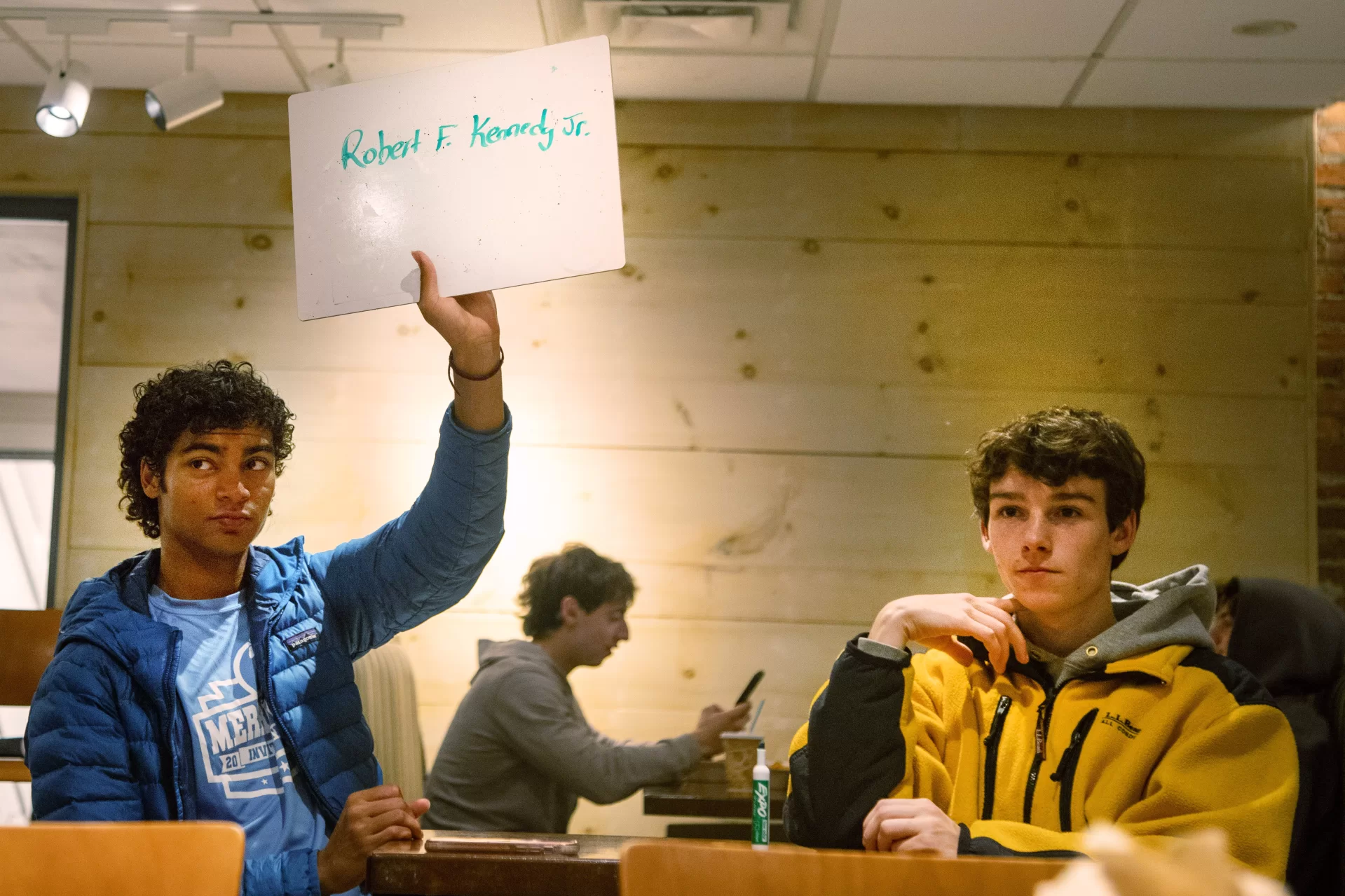 a student holding a sign with a trivia answer with a friend next to him.