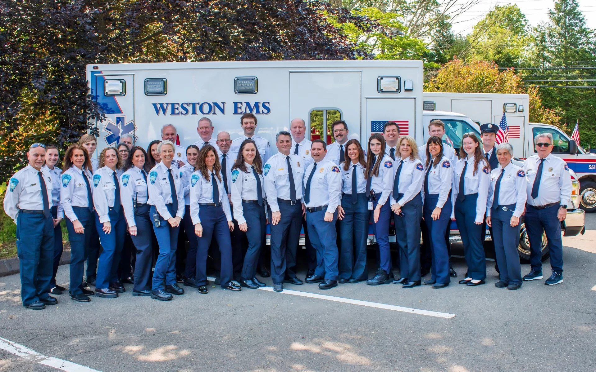 large group of EMTs in uniform front of ambulance