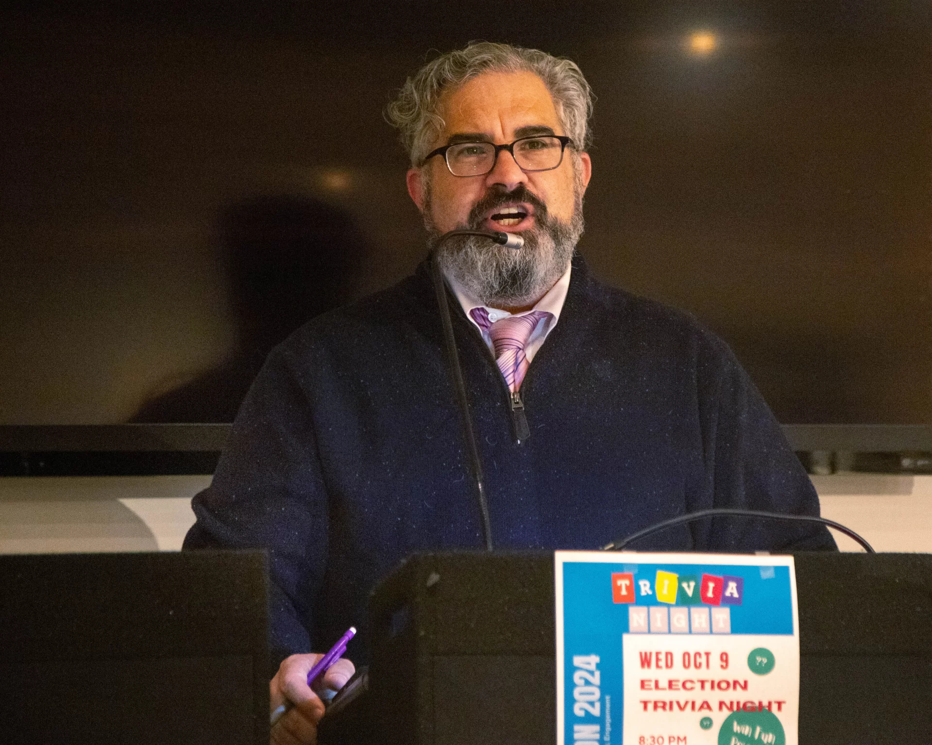 professor at lectern reading questions for trivia night