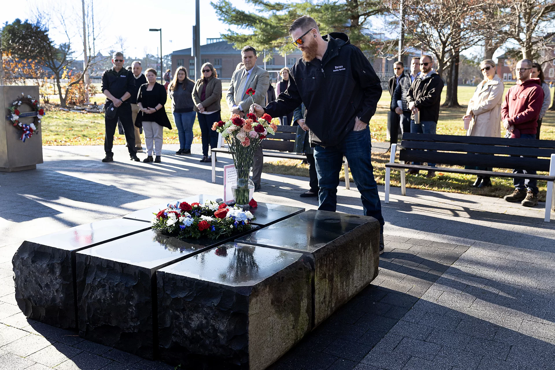 On Veterans Day, we pause to reflect and remember.

During this morning’s gathering at Bates Veterans Plaza, Joe Castonguay of Facility Services lays a flower atop one of the basalt stones that comprise the plaza centerpiece. “I learned the value of human life in combat,” said Castonguay, a U.S. Army veteran who served for 15 months in Iraq.

The Rev. Dr. Brittany Longsdorf, @bates_multifaith chaplain, guided today’s centering moment, which included reflective readings and interfaith prayers, the observing of silence, and the ritual of laying flowers to honor the service and sacrifice of veterans.

Dedicated in 2020 and located near the Benjamin E. Mays Center, the plaza honors Bates veterans and invites “reflection on the impact of war on the lives of everyone it touches.”

President Garry W. Jenkins was in attendance.