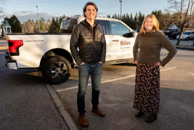 When the Bates student EcoReps encounter a sustainability problem that needs solving, they don’t just sit around and debate solutions — they envision and then execute them. In two of their most recent successes, the students helped to secure funding to solve an unexpected problem with the existing electric vehicle chargers on campus and helped purchase a slew of new EVs for campus use. “It's really cool that as students, I feel like we have a voice,” says Martin Carriere ’25, an EcoRep from Davis, Calif. “I always feel like our ideas are heard. We're positioned to have bolder ideas and be able to bring those to the table.” Bates is known for its impressive achievements in sustainability, but the existential threat of climate change gives expanding the work great urgency. Carriere, a double major in politics and environmental studies, and fellow EcoRep Cassidy Meyer ’25, an environmental studies major from Carbondale, Co., are both set to graduate this month — and both are working on sustainability solutions right until the end. They even had a meeting on local renewable energy scheduled with college leaders during their last week of classes, amid the haze of studying for finals and saying goodbyes. The two pose for a portrait with the F-150 EV truck outside of Cutten Maintenance Center. And in one photograph, they pose with Paint Shop supervisor Tom Tom Espeaignnette.