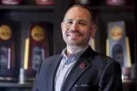 Jason Fein, Athletics Director, poses outside of Alumni Gym and in its lobby.