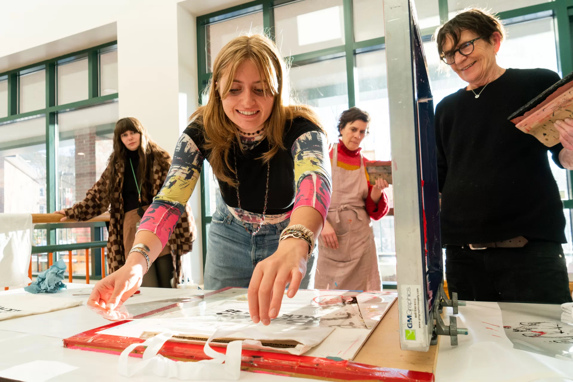 January 20, 2025 - January 20, 2025 - Professor Michel Droge(in black) and Professor Cat Balco (in pink) lead a Screen Printing Drop-In Workshop relating to the college’s 2025 MLK Day theme, Bending Toward Justice: Peace and Nonviolence. T-Shirts and Tote bags were available for attendees to screen print one of the student created designs. 

Professor Droge helped Emmy Comrack '25 through printing a Bates MLK Day '25 design on a totebag.