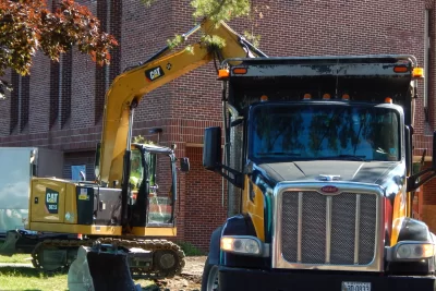 An excavator and dump truck are being used to remove a driveway that’s no longer needed in front of 96 Campus Avenue. (Doug Hubley/Bates College)