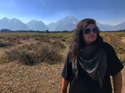 Person with sunglasses and dark tshirt with mountains in the background